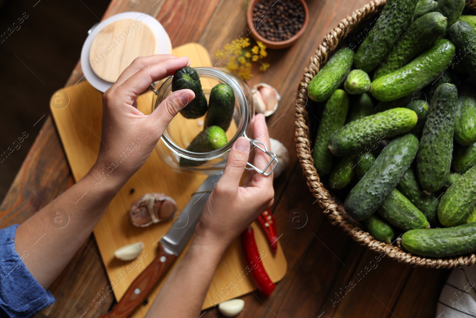 Photo of Woman putting cucumbers into jar at wooden table, top view. Pickling vegetables