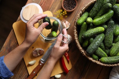 Photo of Woman putting cucumbers into jar at wooden table, top view. Pickling vegetables