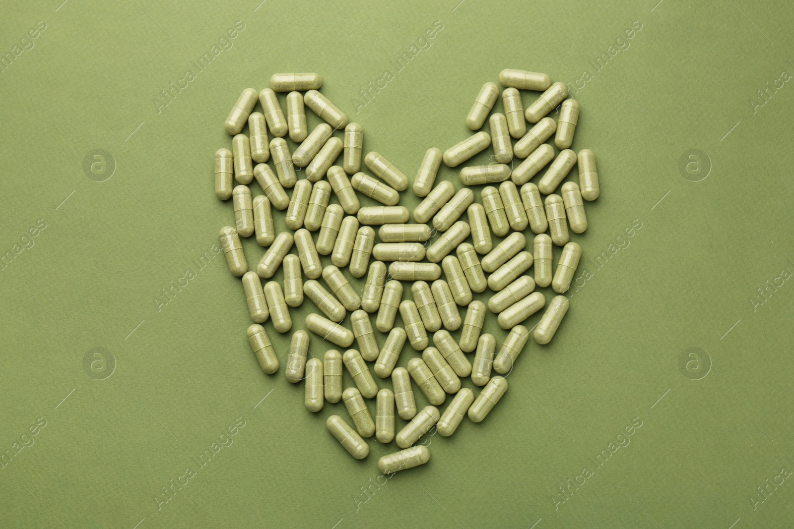 Photo of Heart made of vitamin capsules on olive background, top view