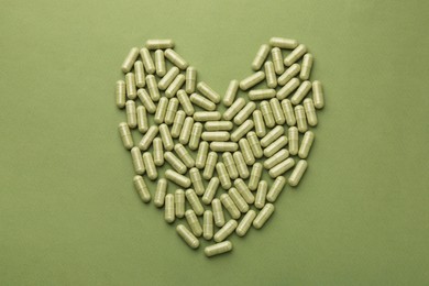 Heart made of vitamin capsules on olive background, top view