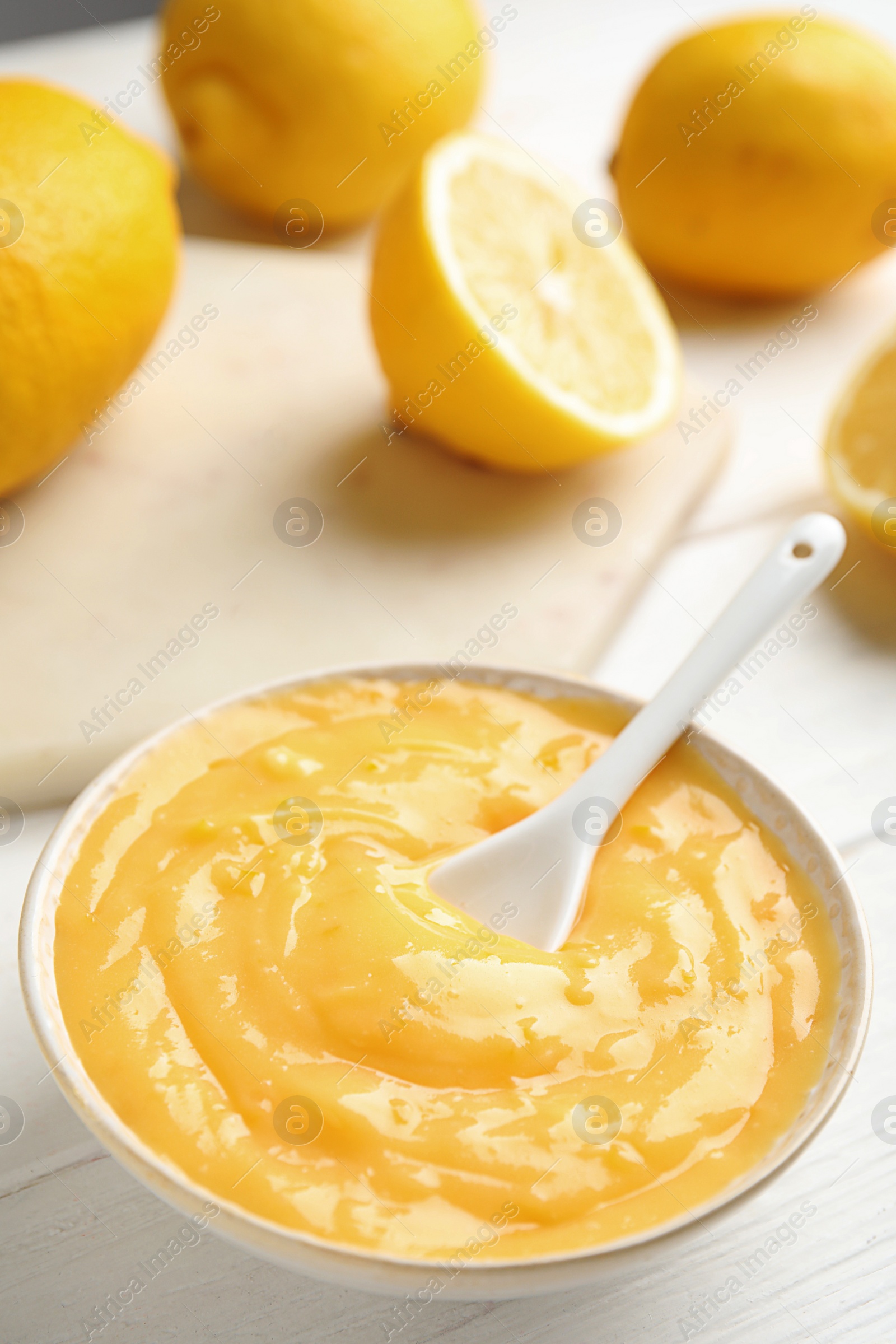 Photo of Delicious lemon curd in bowl on white wooden table. Space for text