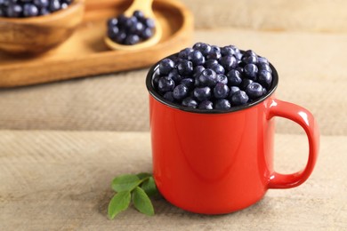 Red mug of tasty fresh bilberries on wooden table, closeup. Space for text