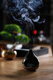 Photo of Incense sticks smoldering on wooden table indoors