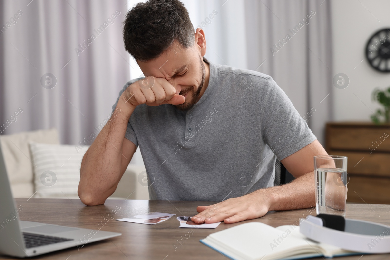 Photo of Crying man with parts of photo sitting at table indoors. Divorce concept