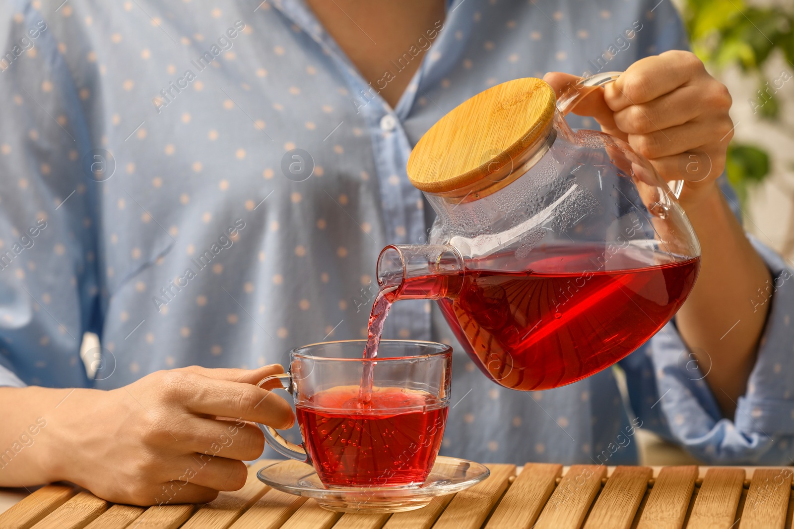 Photo of Woman pouring delicious hibiscus tea into cup at wooden table, closeup