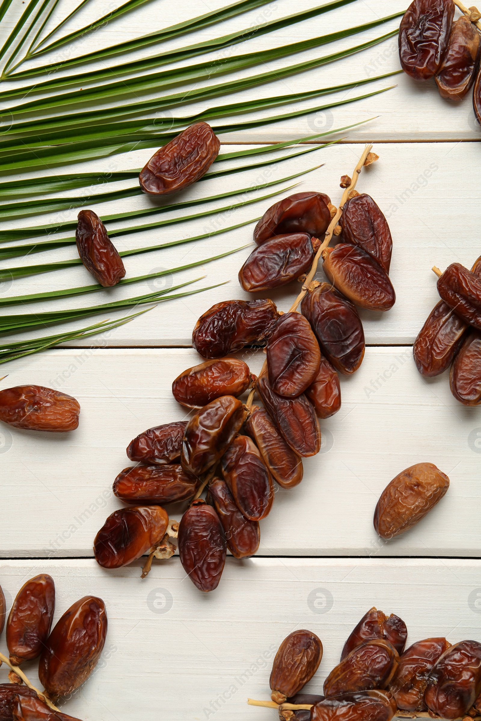 Photo of Sweet dried dates with palm leaf on white wooden table, flat lay