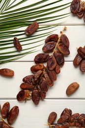 Photo of Sweet dried dates with palm leaf on white wooden table, flat lay