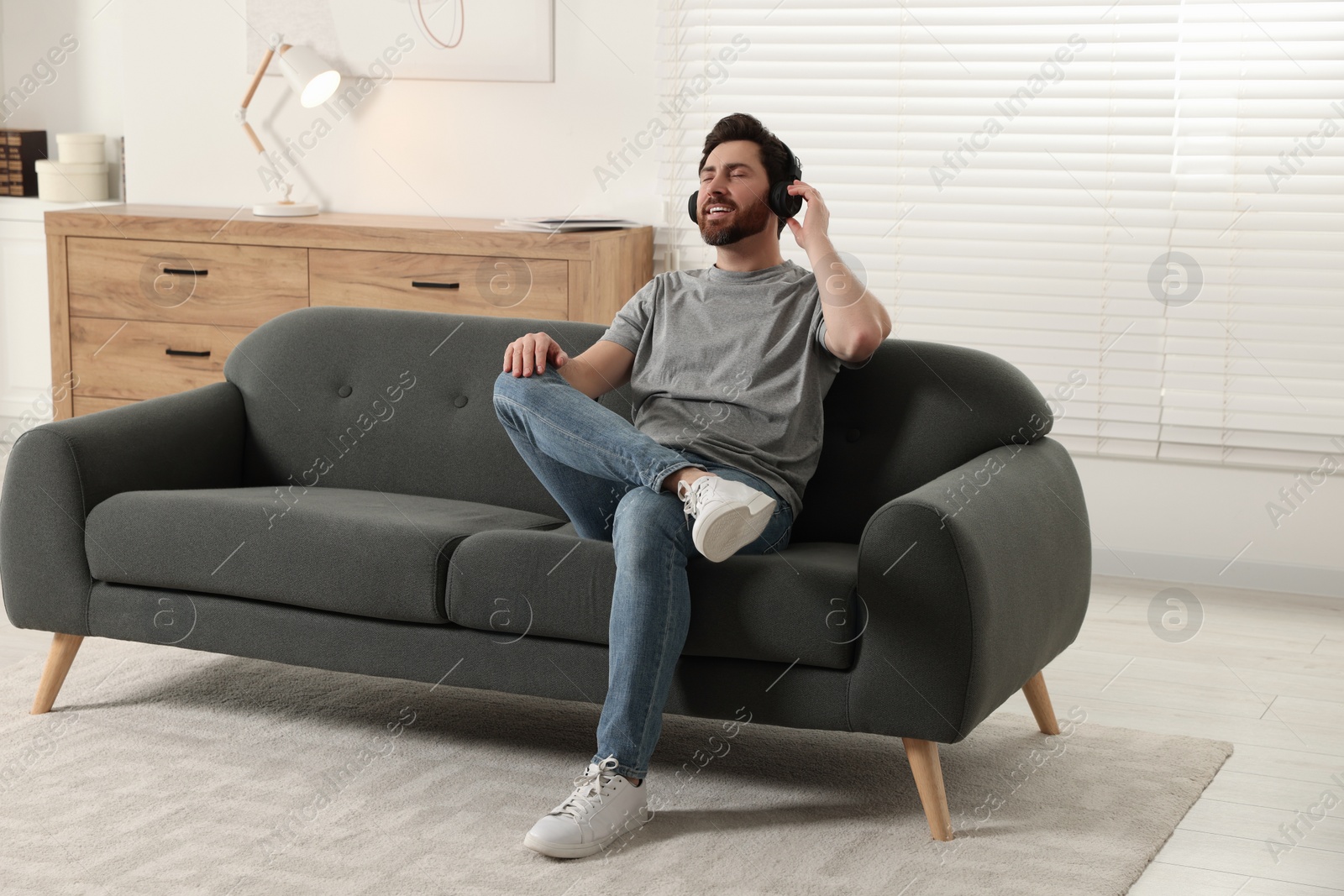 Photo of Happy man listening music with headphones on sofa indoors