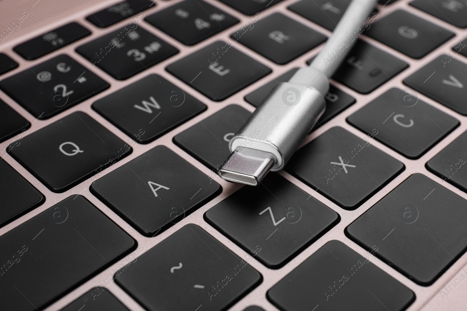 Photo of USB cable with type C connector on laptop keyboard, closeup