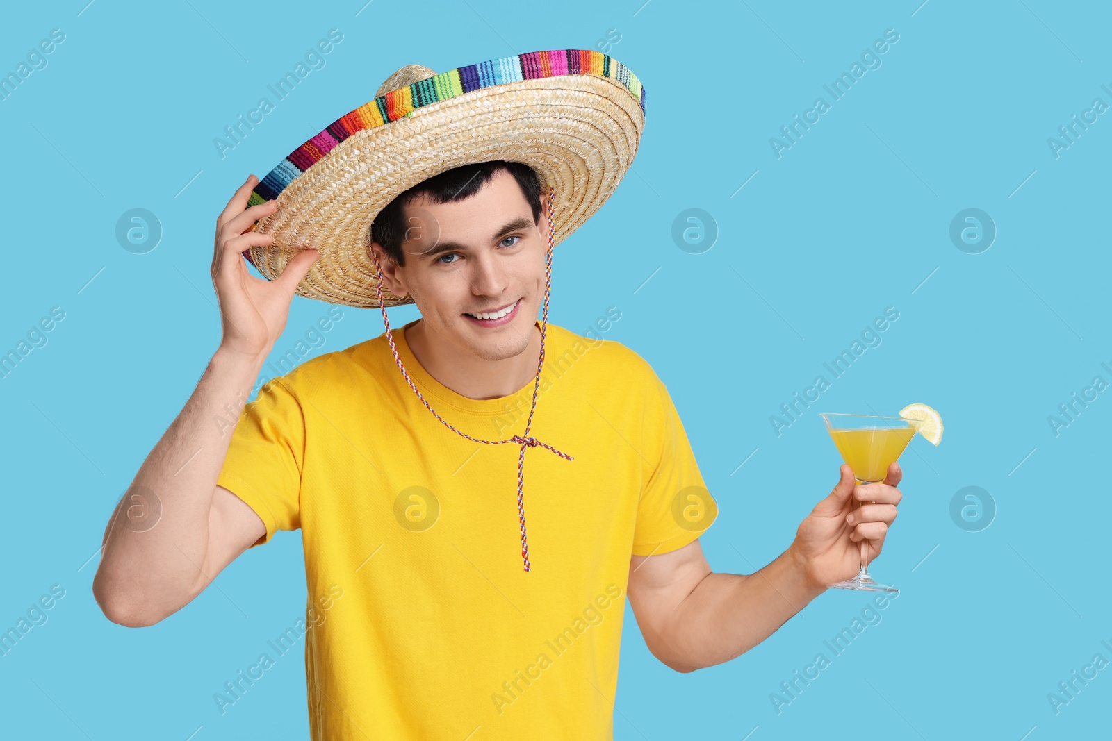 Photo of Young man in Mexican sombrero hat with cocktail on light blue background