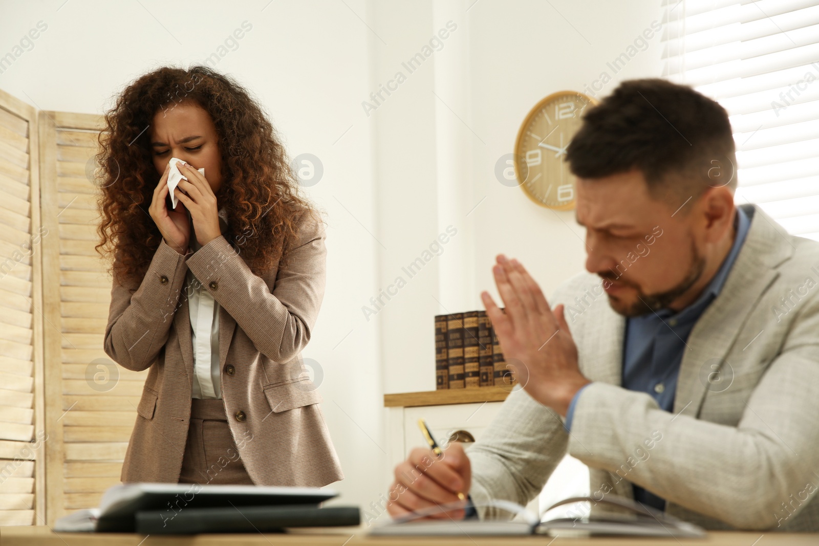 Photo of Sick African-American woman sneezing during meeting in office. Influenza virus