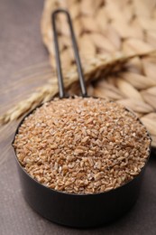 Dry wheat groats in scoop on brown table, closeup
