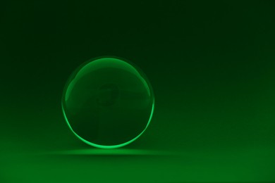 Photo of Transparent glass ball on dark green background. Space for text