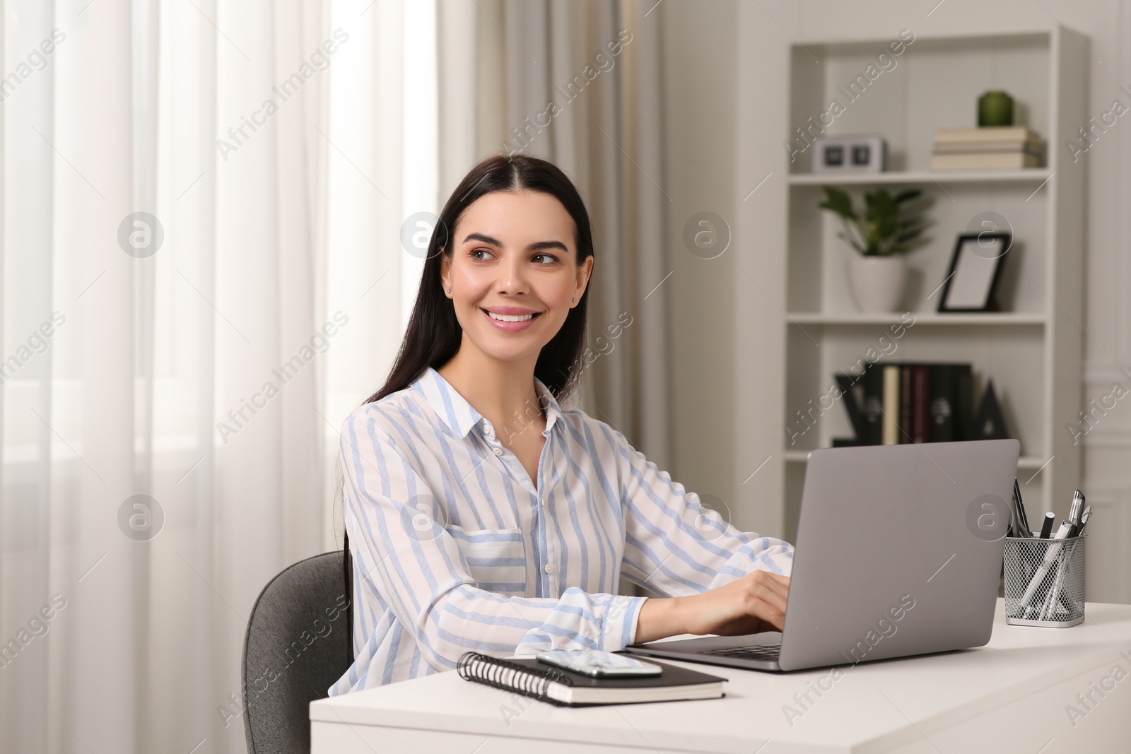 Photo of Happy woman working with laptop at white desk in room