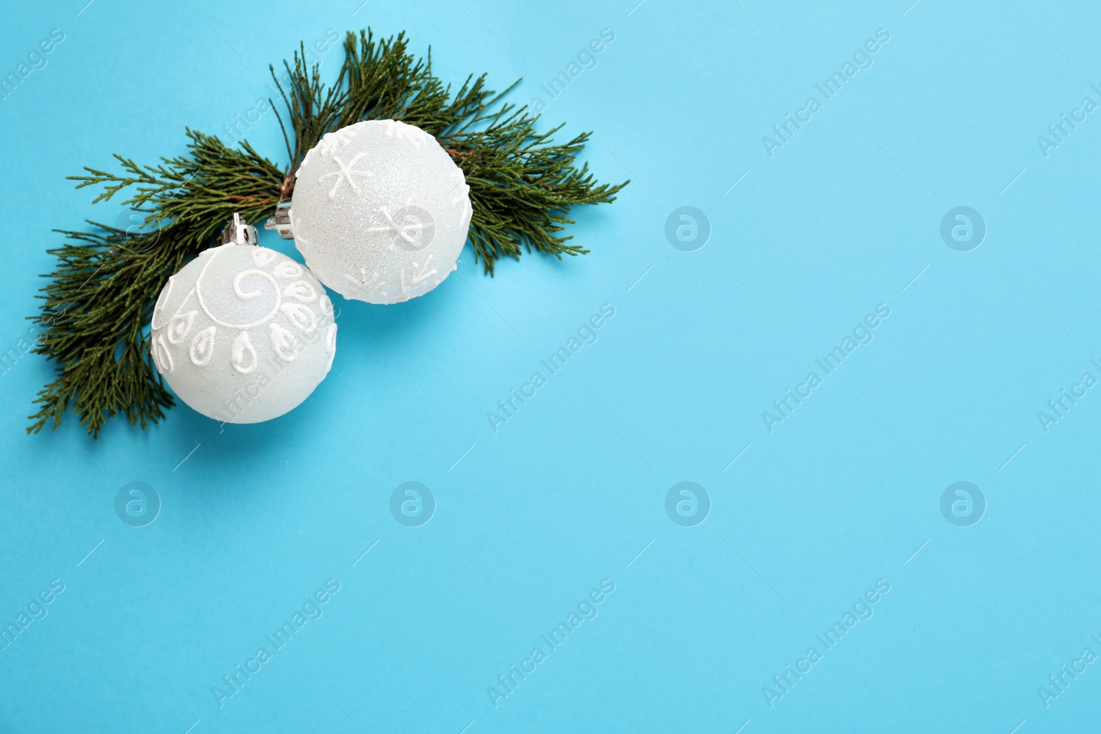 Photo of Beautiful white Christmas balls and fir branches on light blue background, above view. Space for text