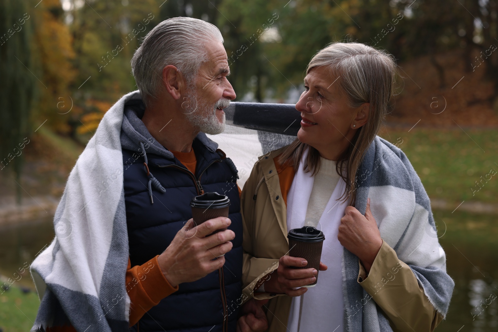 Photo of Affectionate senior couple with cups of coffee in autumn park