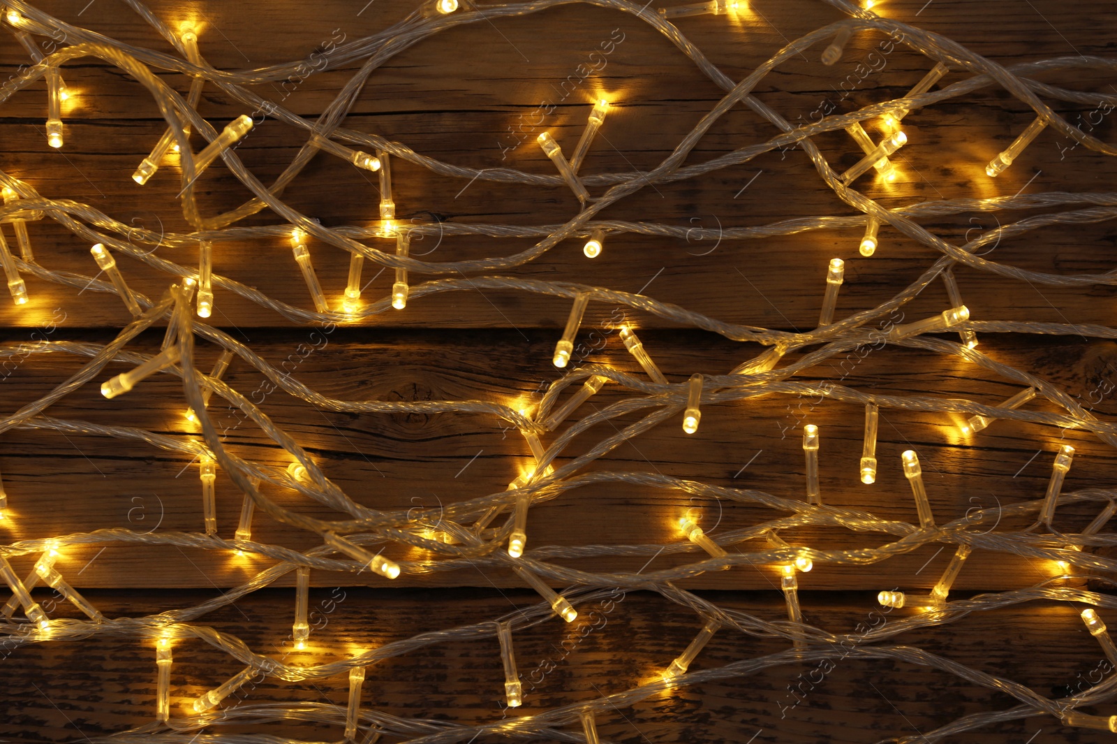 Photo of Glowing Christmas lights on wooden background, top view