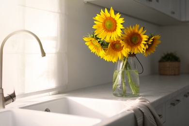 Photo of Vase with beautiful yellow sunflowers in kitchen