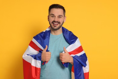Photo of Man with flag of United Kingdom showing thumbs up on yellow background