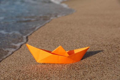 Photo of Orange paper boat on sand near sea, space for text