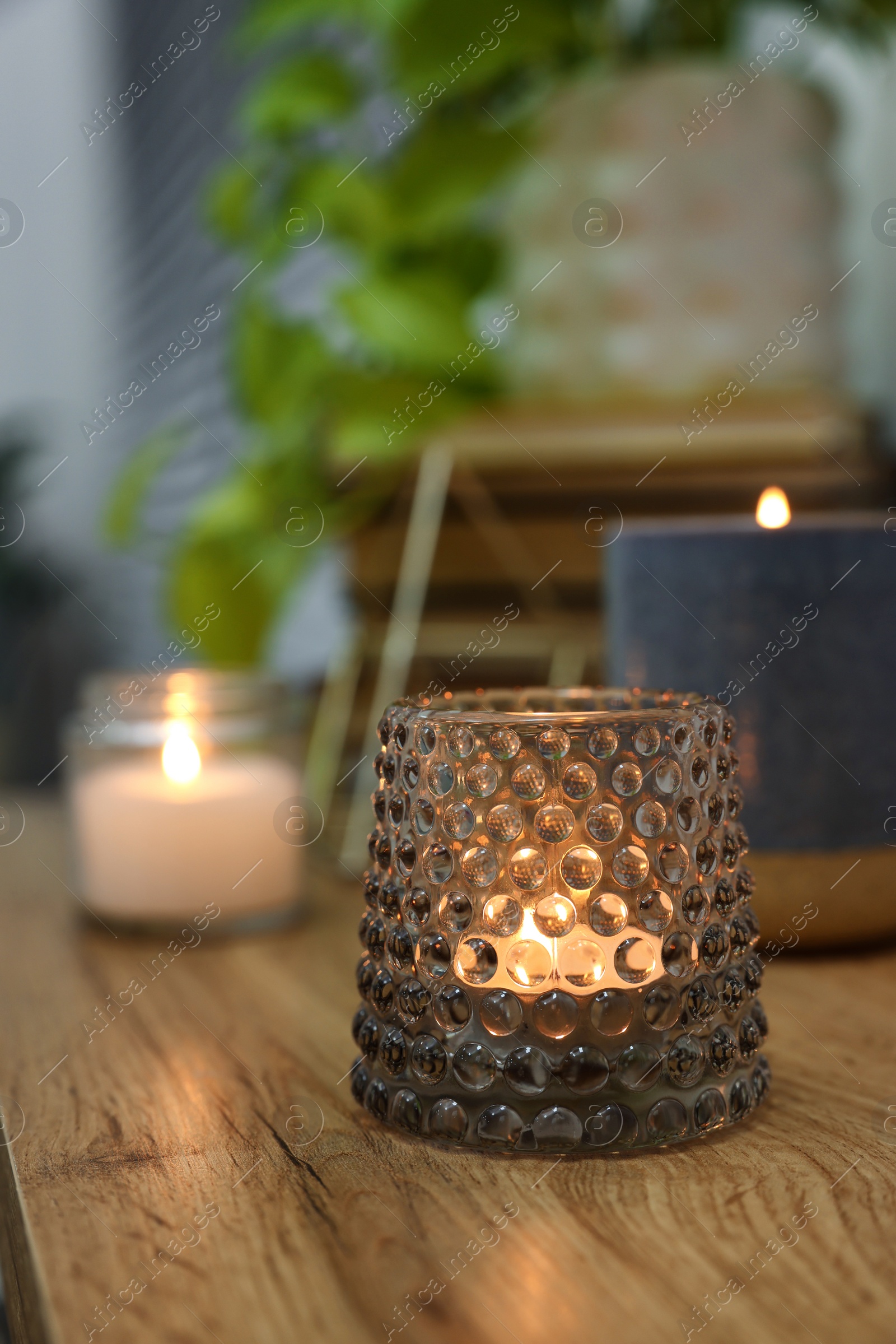 Photo of Lit candles in different holders on wooden table indoors. Space for text