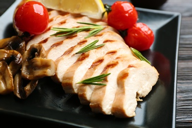 Tasty grilled chicken fillet with mushrooms, tomatoes and rosemary on plate, closeup