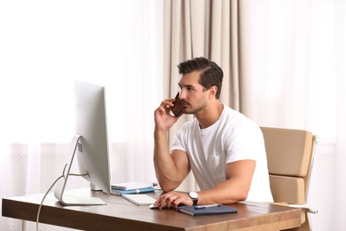 Photo of Handsome young man working with smartphone and computer at table in office