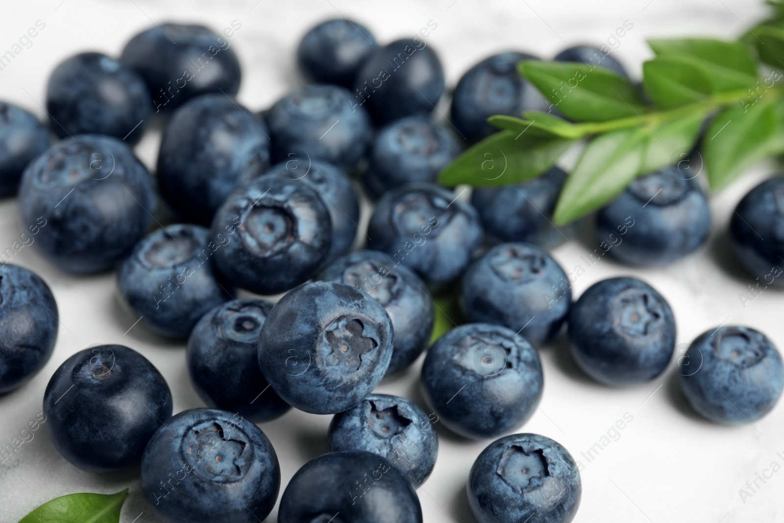 Photo of Pile of tasty fresh blueberries and leaves on light table, closeup