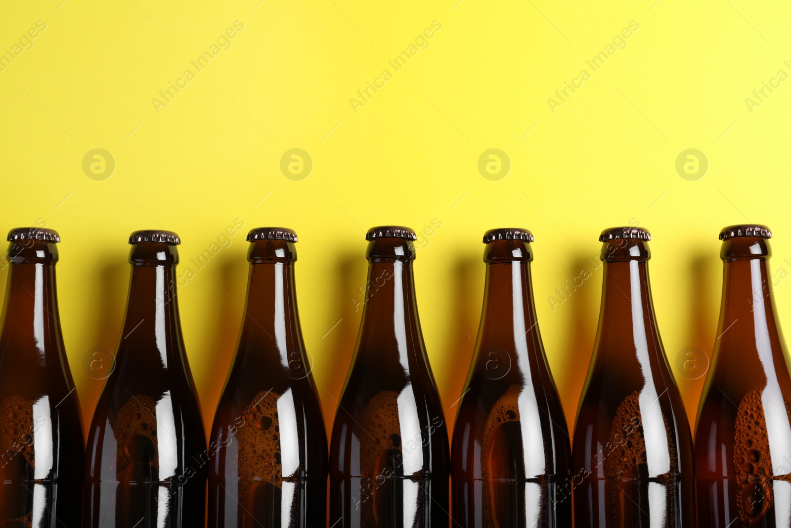 Photo of Bottles of beer on yellow background, flat lay. Space for text