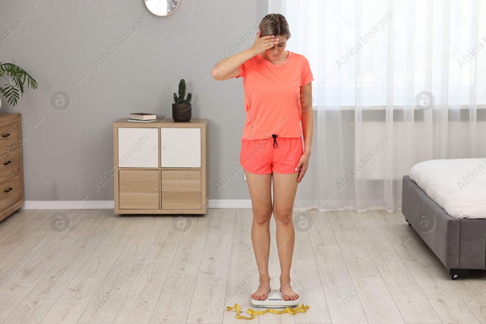 Photo of Woman in sportswear standing on floor scales at home