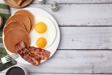 Tasty pancakes served with fried eggs and bacon on white wooden table, flat lay. Space for text