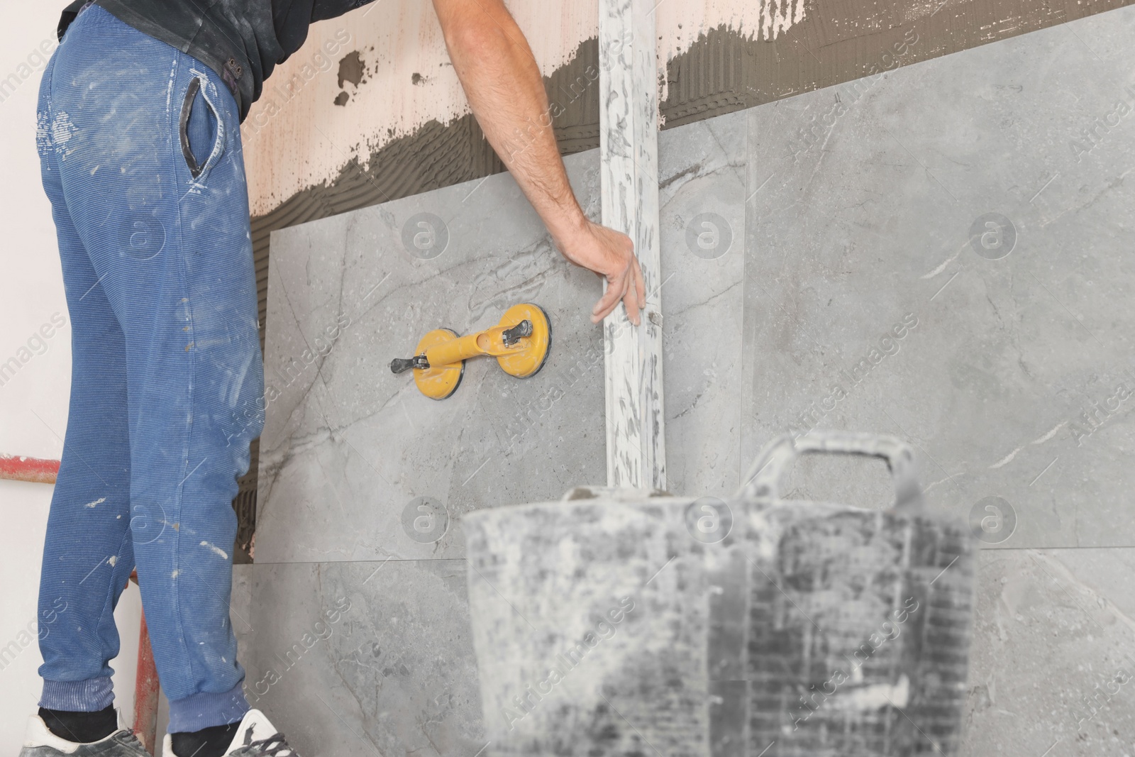 Photo of Worker installing wall tile with vacuum holder indoors, closeup