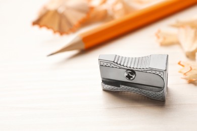Metal sharpener near pencil and shavings on white wooden table, closeup. Space for text