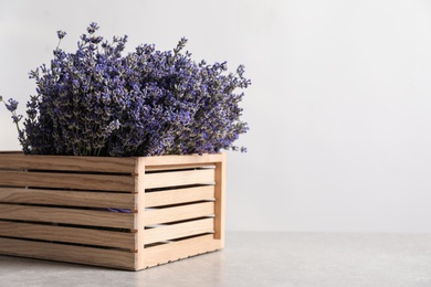 Photo of Fresh lavender flowers in wooden crate on stone table against light background, space for text