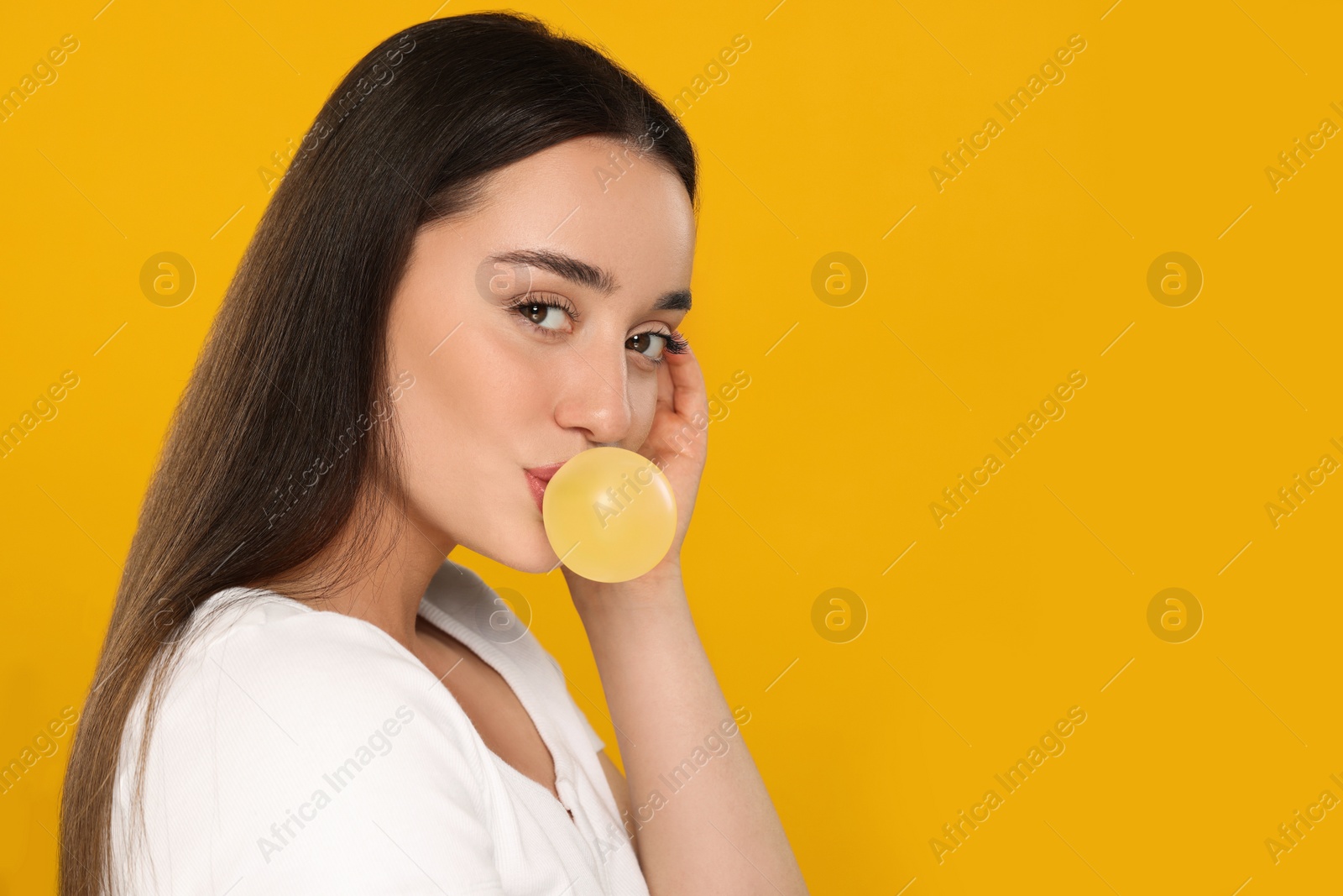 Photo of Beautiful young woman blowing bubble gum on yellow background. Space for text