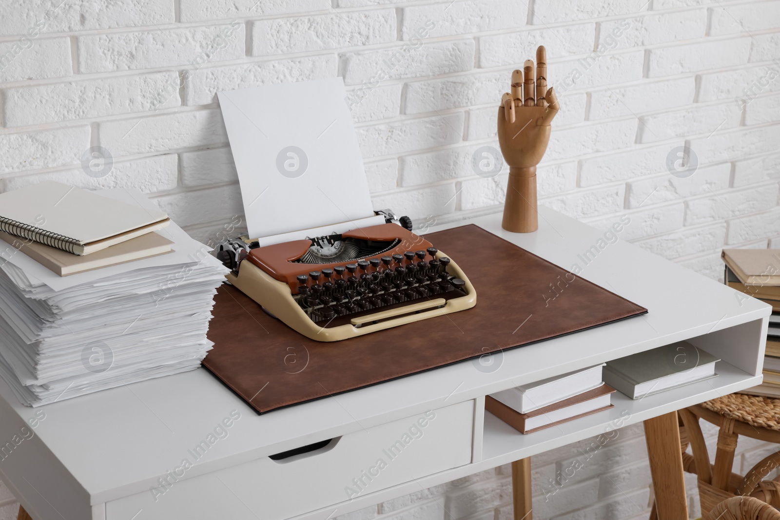 Photo of Comfortable writer's workplace with typewriter on desk near white brick wall