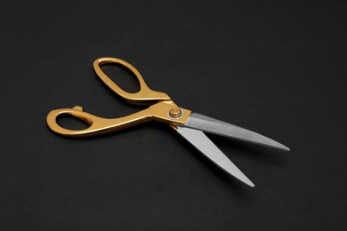 Photo of Stylish gold tailor scissors on black background