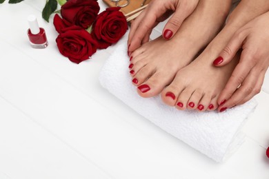 Photo of Woman with stylish red toenails after pedicure procedure and rose flowers on white wooden floor, closeup. Space for text