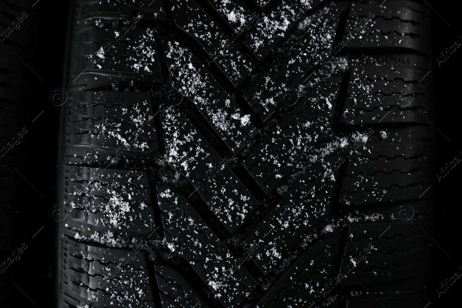 Photo of Snowy winter tire on black background, closeup