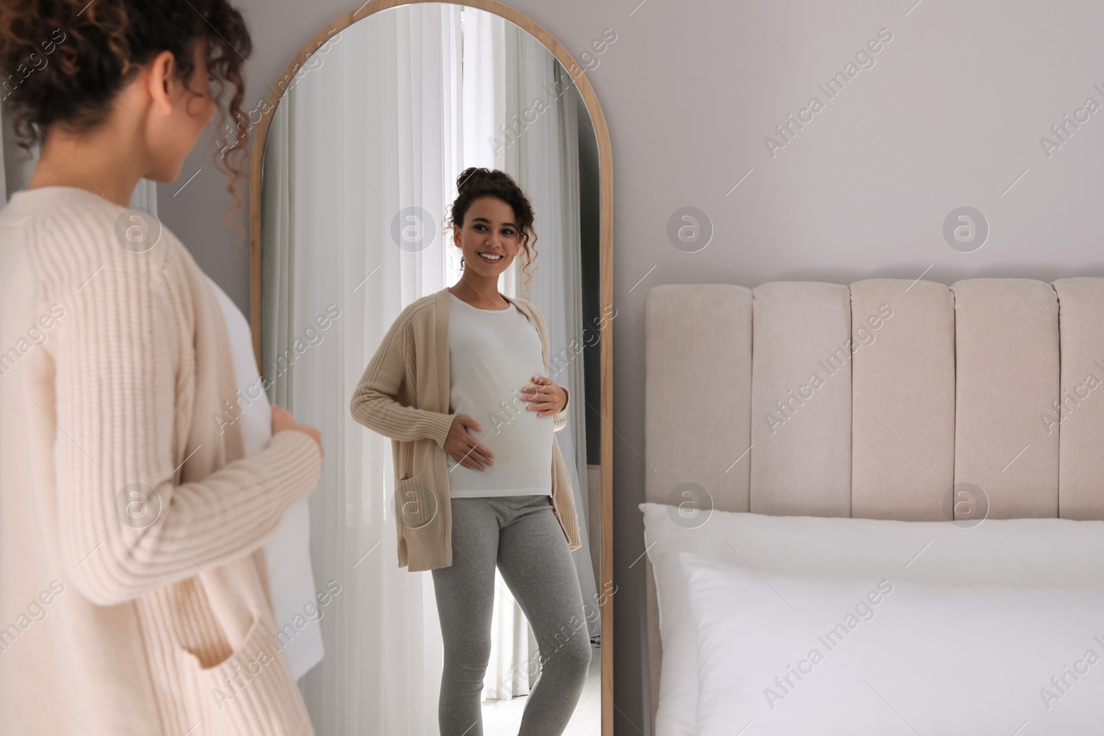 Photo of Pregnant young African-American woman near mirror at home