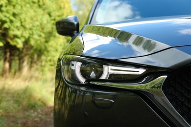 Headlight of modern black car near trees outdoors, closeup