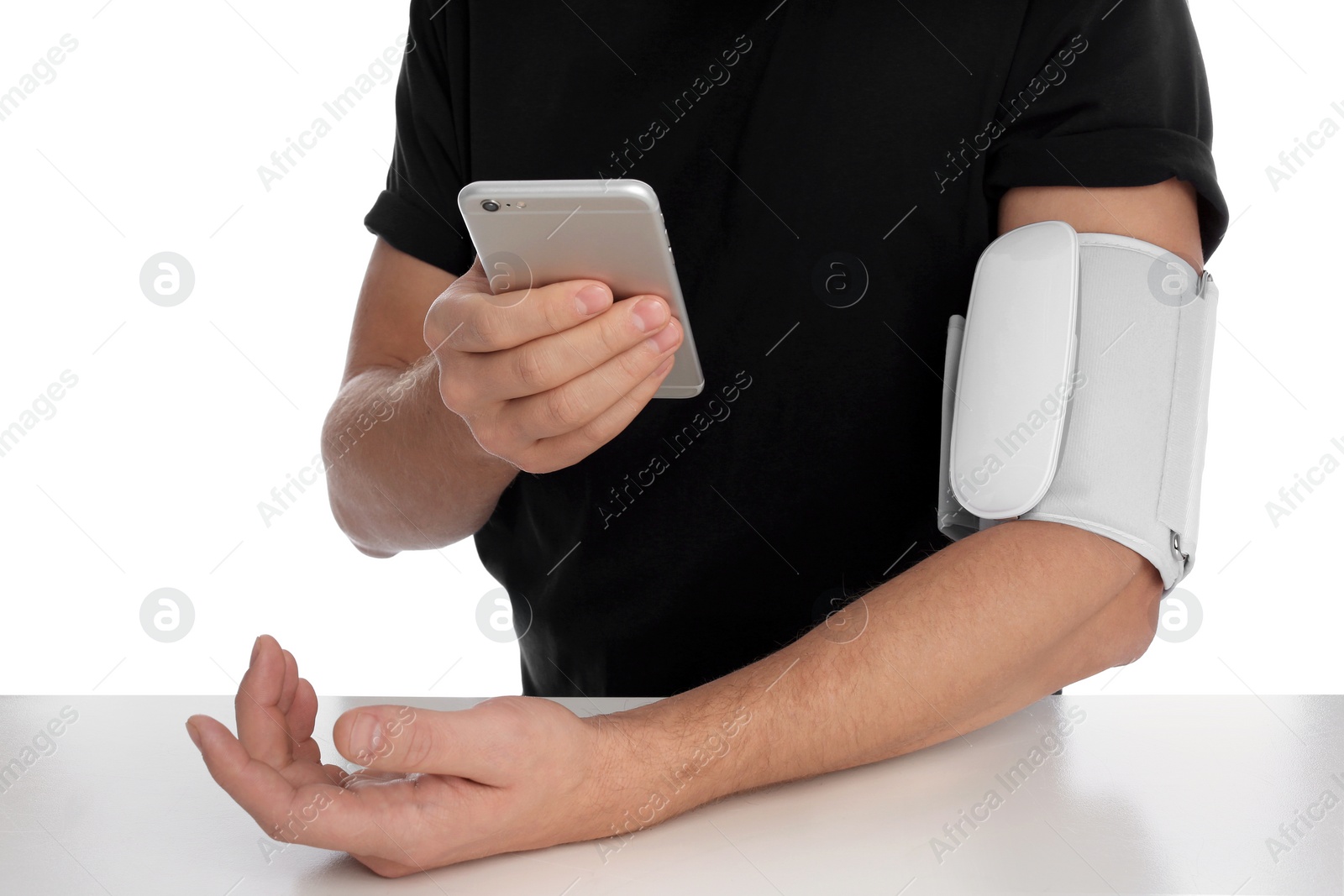 Photo of Man checking blood pressure with modern monitor and smartphone at table against white background, closeup. Cardiology concept