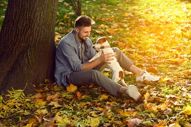 Photo of Man with adorable Jack Russell Terrier in autumn park. Dog walking