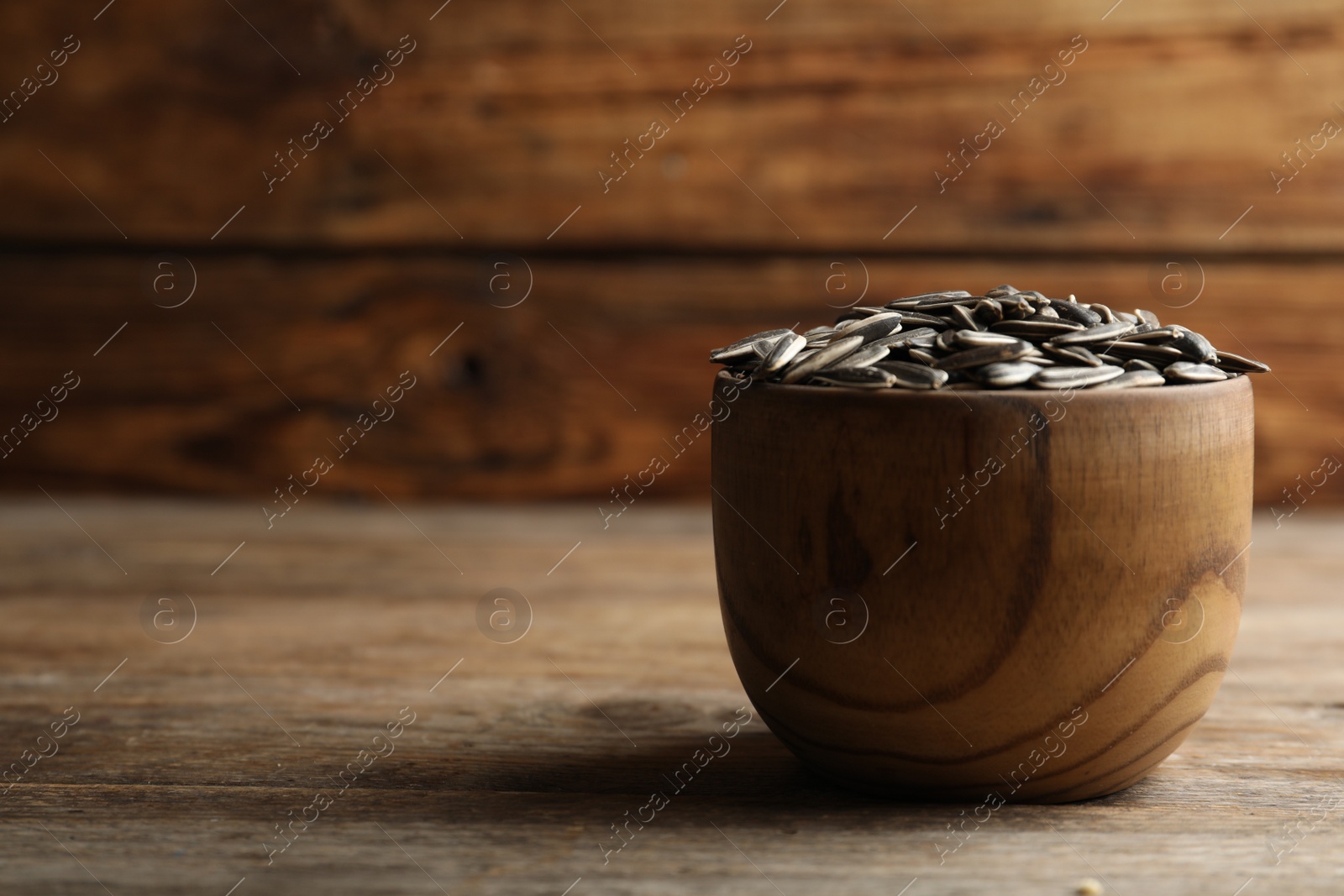 Photo of Raw sunflower seeds in bowl on wooden table. Space for text