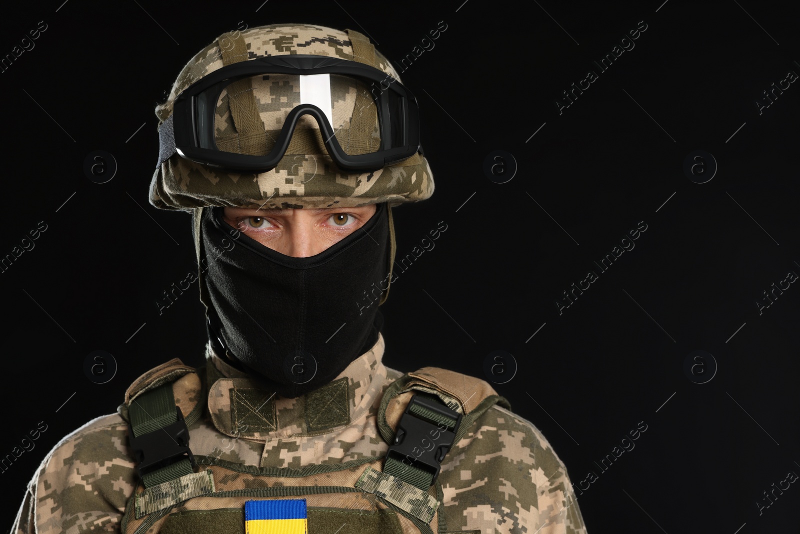 Photo of Soldier in Ukrainian military uniform, tactical goggles and balaclava on black background. Space for text