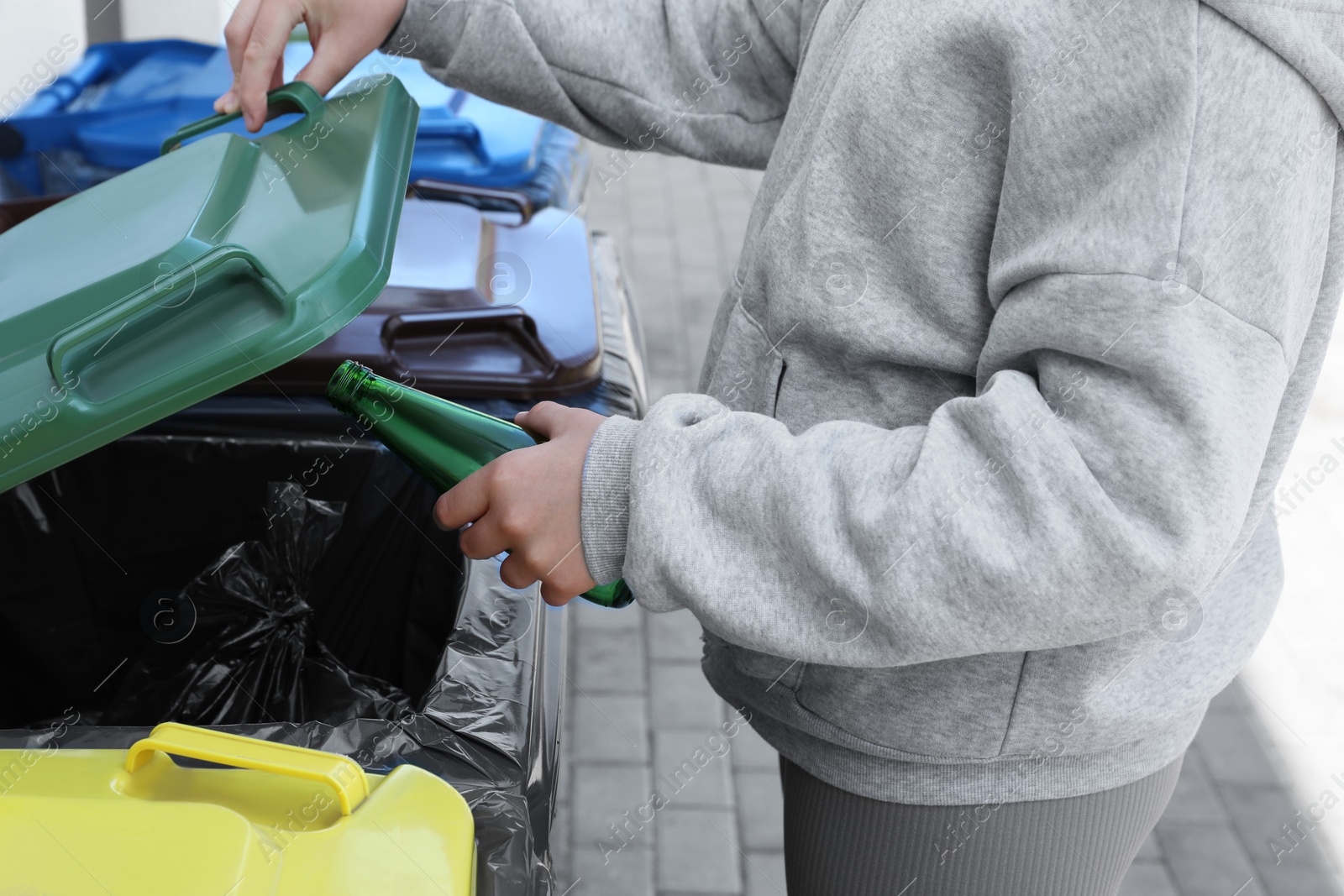 Photo of Woman throwing glass bottle in bin outdoors, closeup. Recycling concept