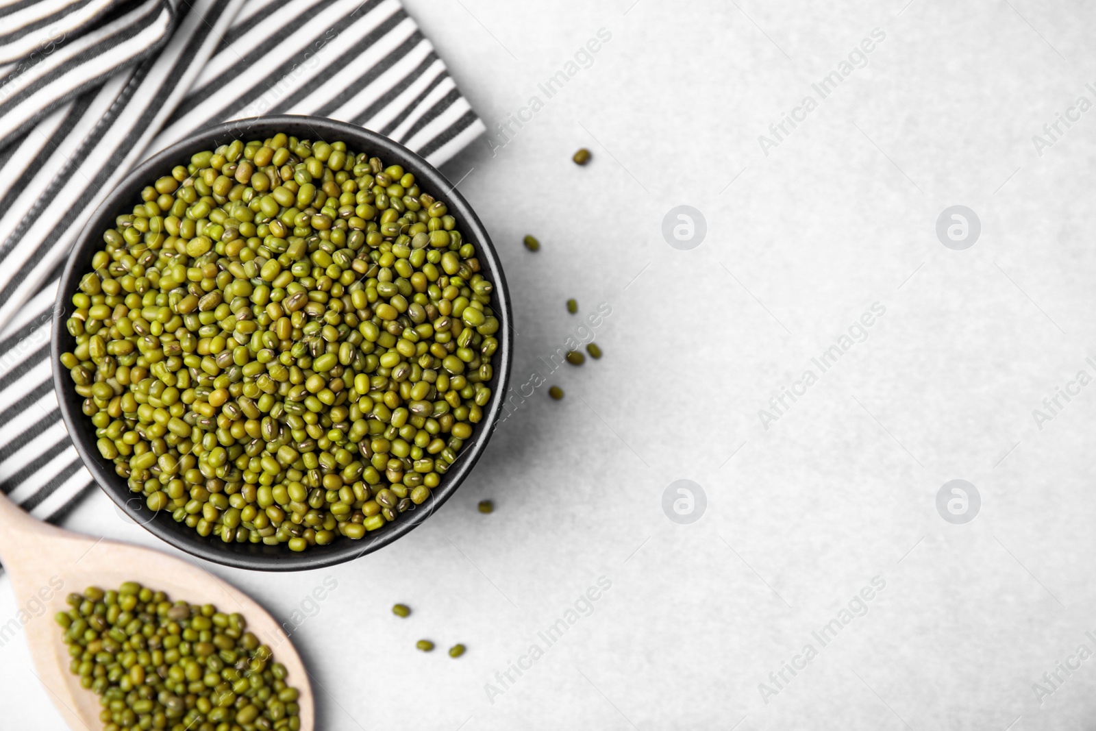 Photo of Bowl and wooden spoon with green mung beans on light grey table, flat lay. Space for text