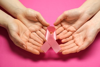 Women holding pink ribbon on color background, closeup. Breast cancer awareness
