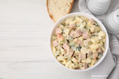 Photo of Tasty Olivier salad with boiled sausage in bowl on white wooden table, top view. Space for text