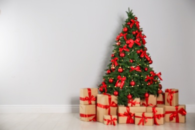 Photo of Blurred view of decorated Christmas tree and gift boxes near light wall. Space for text